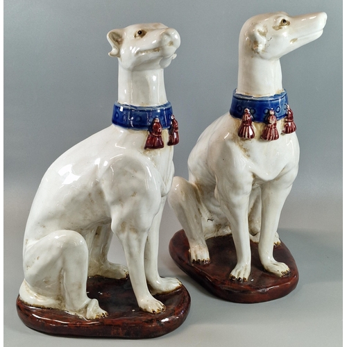 126 - Pair of continental pottery studies of seated hounds with tasselled collars, on oval natural bases. ... 