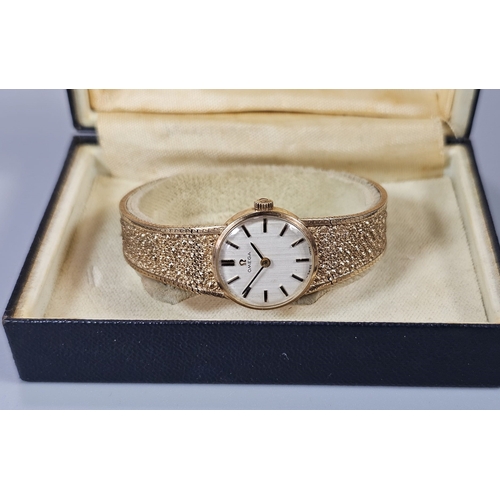 457 - 9ct gold Omega bracelet wristwatch, having circular satin face with Baton numerals on a bark finish ... 