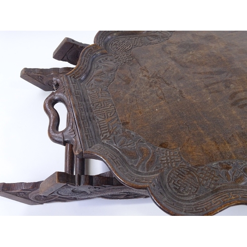 87 - A Chinese hardwood 2-handled tea tray on folding stand, with relief carved dragon and symbolic decor... 