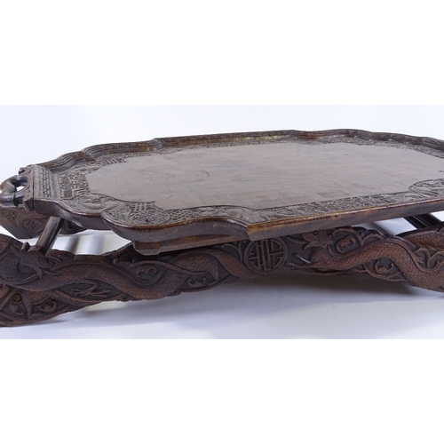 87 - A Chinese hardwood 2-handled tea tray on folding stand, with relief carved dragon and symbolic decor... 