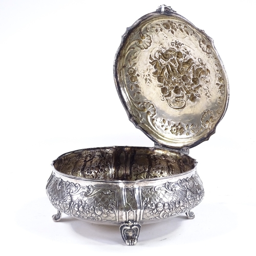 613 - A large German circular silver box, with hinged lid, on scrolled acanthus leaf feet, relief embossed... 