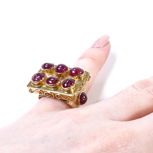 486 - An Eastern unmarked gold cabochon ruby cluster panel ring, scrollwork border and ribbed cabochon rub... 