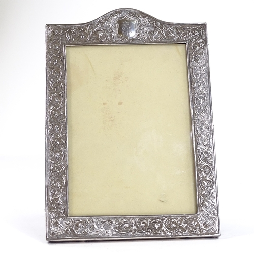 709 - An Indian unmarked silver-fronted photo frame, with relief embossed foliate decoration and hardwood ... 