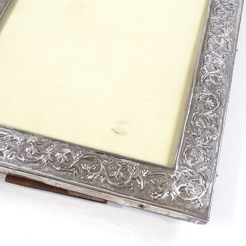 709 - An Indian unmarked silver-fronted photo frame, with relief embossed foliate decoration and hardwood ... 