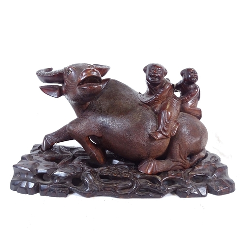 228 - An Oriental hardwood figure of 2 boys riding a water buffalo, on fitted carved and pierced stand, st... 