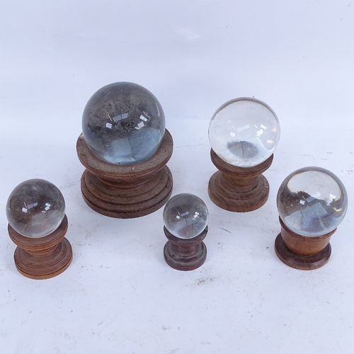 404 - A graduated set of 5 clear glass crystal balls on wood stands, largest and smallest diameters 10cm a... 