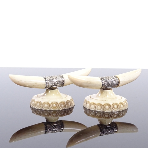 128 - A pair of ivory and silver knife rests, in the form of horns and carved base, width 7cm.