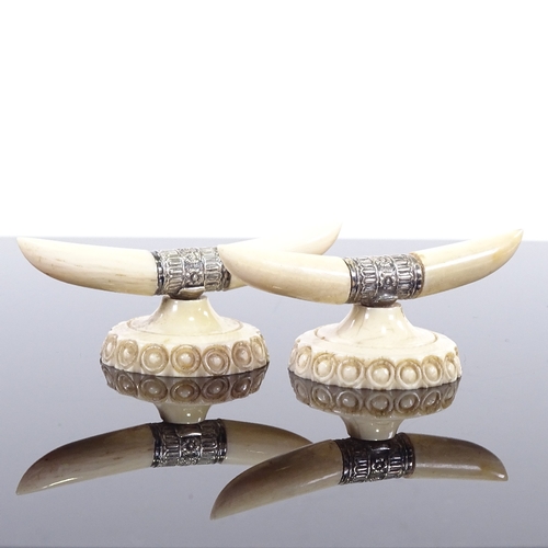 128 - A pair of ivory and silver knife rests, in the form of horns and carved base, width 7cm.