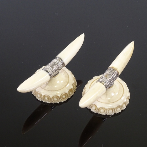 128 - A pair of ivory and silver knife rests, in the form of horns and carved base, width 7cm.