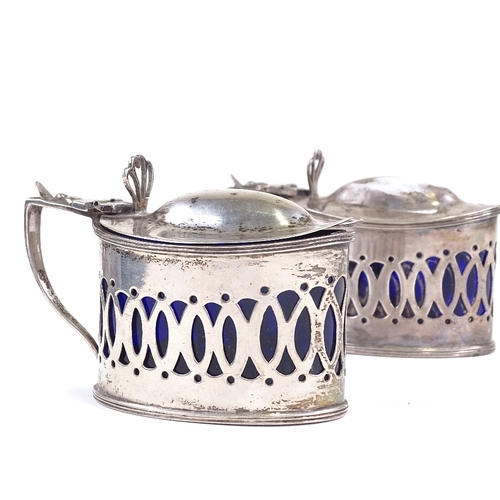 628 - A pair of late Victorian silver mustard pots, pierced decoration with blue glass liners and heart th... 