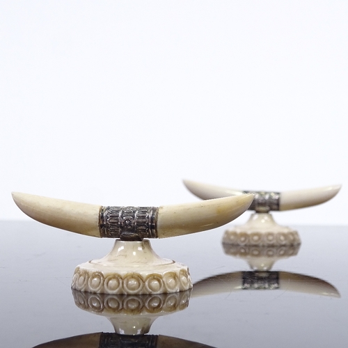 212 - A pair of ivory and silver knife rests, in the form of horns and carved base, width 7cm.