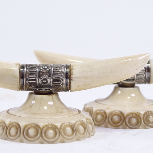 212 - A pair of ivory and silver knife rests, in the form of horns and carved base, width 7cm.