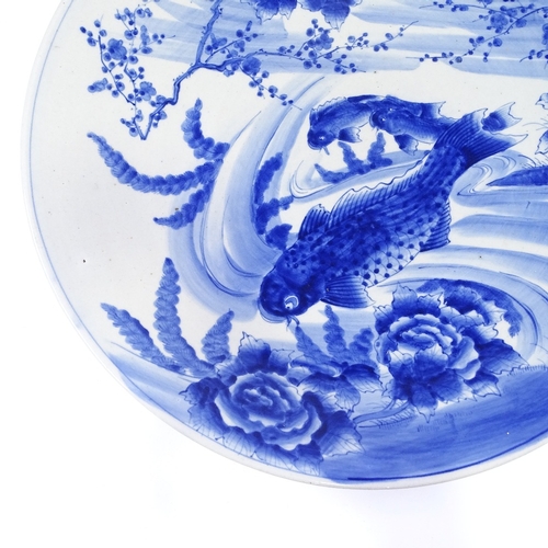 322 - A large Japanese blue and white porcelain charger, with hand painted carp design, diameter 61cm (A/F... 