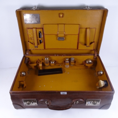 562 - An early 20th century leather suitcase, with partial fitted interior, including glass jars, cut thro... 