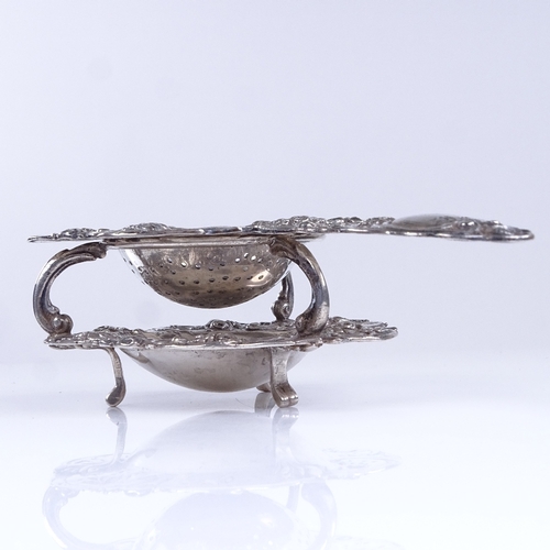 791 - A 19th century German silver tea strainer and matching base, allover relief embossed floral and foli... 