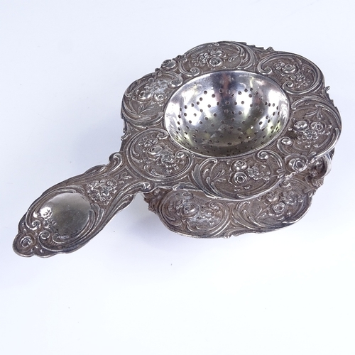 791 - A 19th century German silver tea strainer and matching base, allover relief embossed floral and foli... 