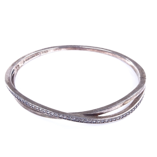 861 - PANDORA - a modern sterling silver and CZ crossover hinged bangle, band width 6.4mm, internal dimens... 