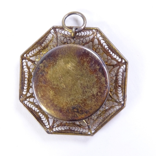 488 - A religious reliquary pendant in unmarked metal filigree surround, 32mm across, leather case