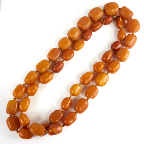 1221 - A long graduated single row butterscotch amber barrel bead necklace, beads measuring from 26.5mm to ... 