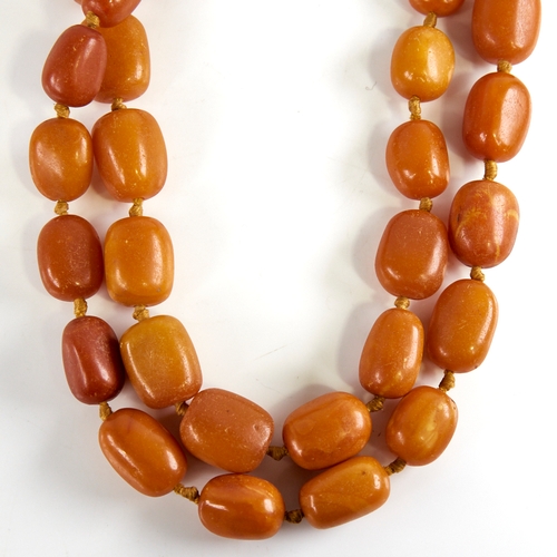 1221 - A long graduated single row butterscotch amber barrel bead necklace, beads measuring from 26.5mm to ... 