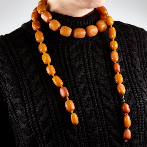 1221 - A long graduated single row butterscotch amber barrel bead necklace, beads measuring from 26.5mm to ... 