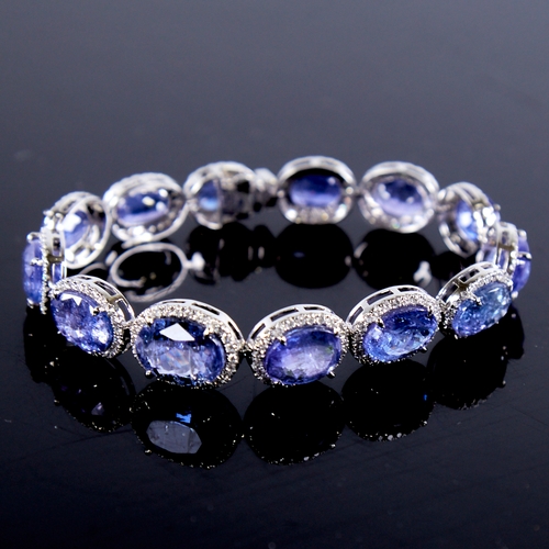 1329 - A modern platinum tanzanite and diamond cluster line bracelet, set with graduated panels of oval-cut... 