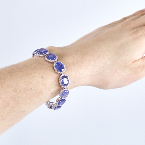 1329 - A modern platinum tanzanite and diamond cluster line bracelet, set with graduated panels of oval-cut... 