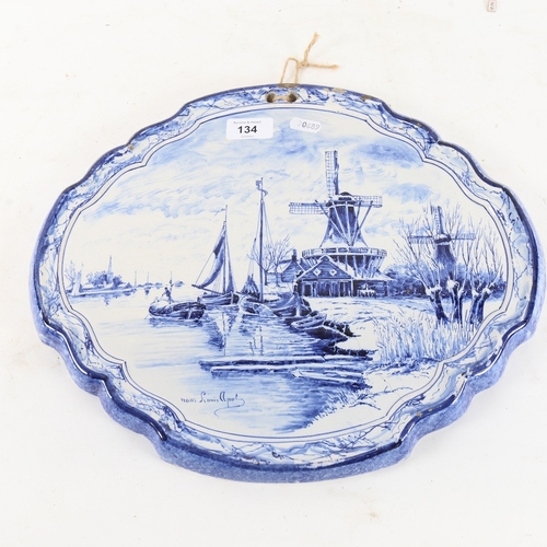 134 - An early 20th century Dutch Delft tin-glaze blue and white plaque, depicting riverside windmills, by... 