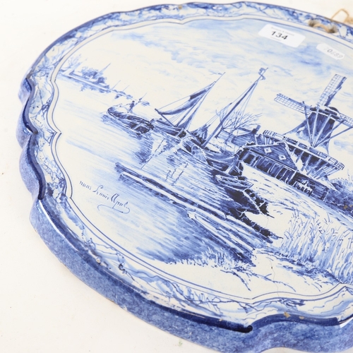 134 - An early 20th century Dutch Delft tin-glaze blue and white plaque, depicting riverside windmills, by... 