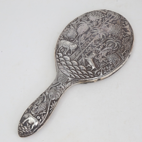 1124 - An unmarked Indian silver dressing table hand mirror, allover relief embossed animal and jungle deco... 