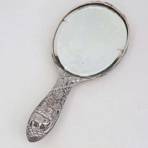 1124 - An unmarked Indian silver dressing table hand mirror, allover relief embossed animal and jungle deco... 