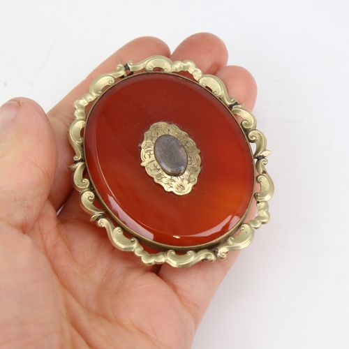 1139 - A large Victorian oval mourning brooch, unmarked yellow metal settings with red banded agate and vac... 