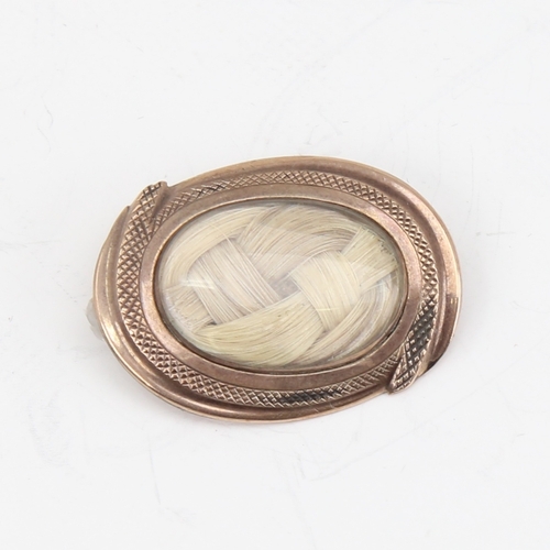 1145 - A small Georgian oval mourning brooch, unmarked gold settings with woven hair panel under convex gla... 