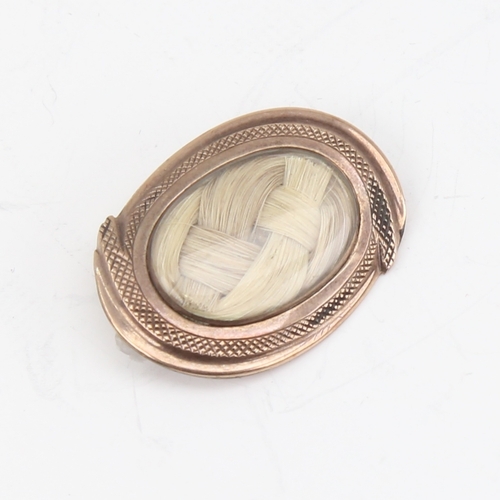 1145 - A small Georgian oval mourning brooch, unmarked gold settings with woven hair panel under convex gla... 