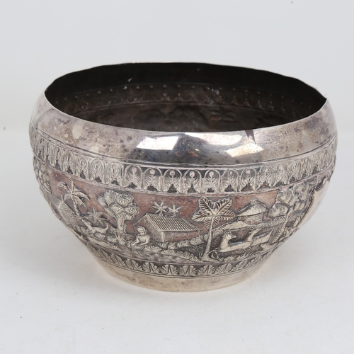 1200 - An early 20th century large Burmese silver rice bowl, relief embossed lion hunting and village scene... 