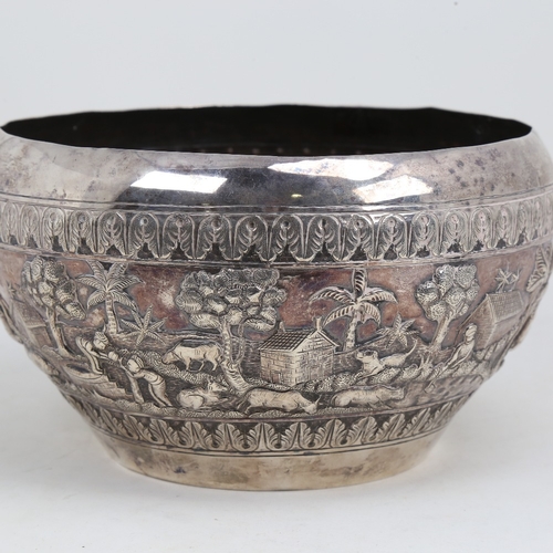 1200 - An early 20th century large Burmese silver rice bowl, relief embossed lion hunting and village scene... 