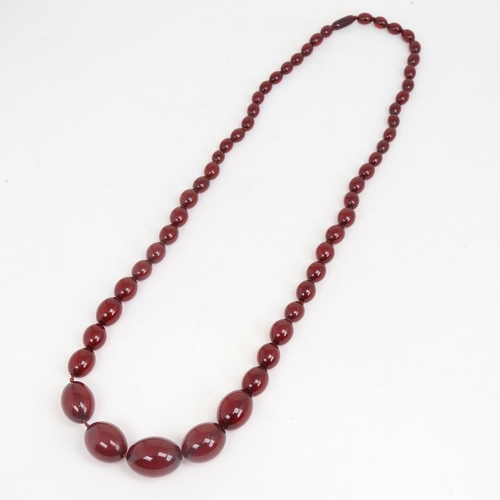 1214 - A long graduated single-strand cherry amber bead necklace, beads measuring from 31.4mm to 12.2mm, ne... 