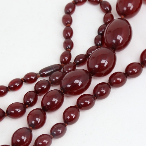 1214 - A long graduated single-strand cherry amber bead necklace, beads measuring from 31.4mm to 12.2mm, ne... 