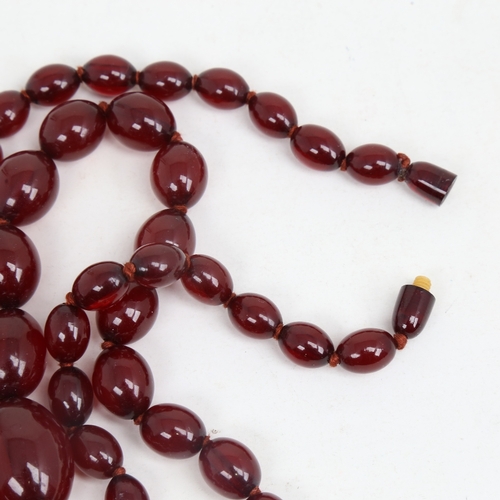 1214 - A long graduated single-strand cherry amber bead necklace, beads measuring from 31.4mm to 12.2mm, ne... 