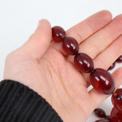 1214 - A long graduated single-strand cherry amber bead necklace, beads measuring from 31.4mm to 12.2mm, ne... 