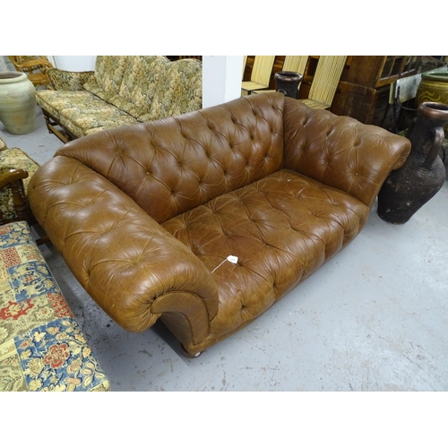 2089 - A buttoned brown leather upholstered Chesterfield settee with rollover arms, on turned stained wood ... 