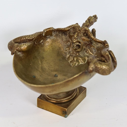 210 - A polished bronze bowl on stand, relief cast serpent and mask designs, length 18cm