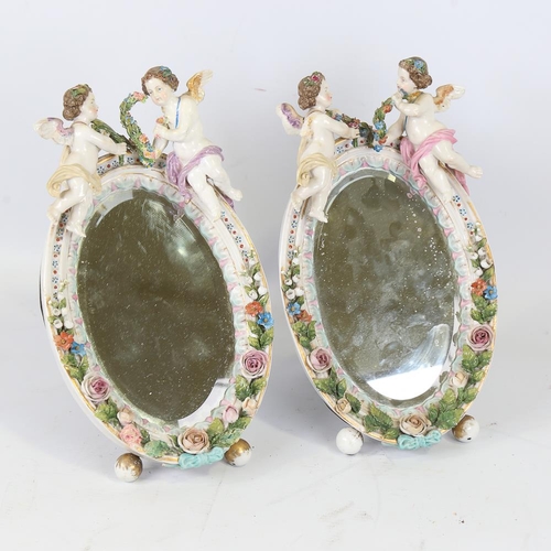 214 - A pair of Continental porcelain framed dressing table mirrors, surmounted by cherub figures, crossed... 