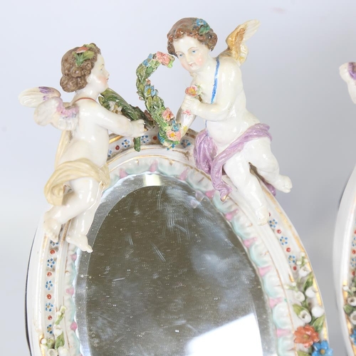 214 - A pair of Continental porcelain framed dressing table mirrors, surmounted by cherub figures, crossed... 