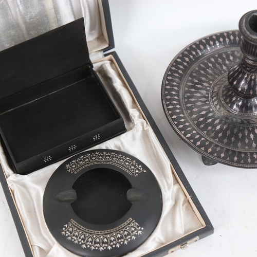 112 - A Middle Eastern silver inlaid oxidised metal candlestick, and a similar cased smoker's set (3)