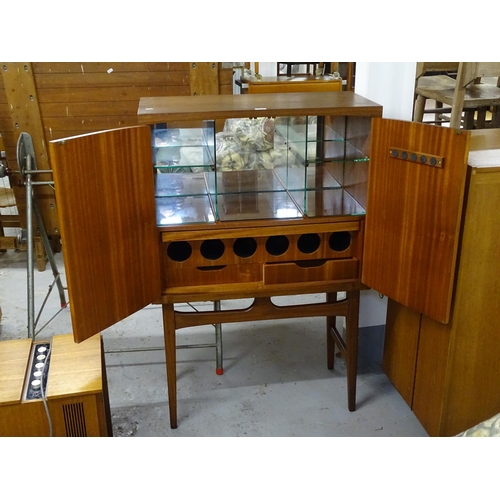 2635 - A mid-century teak cocktail cabinet on stand, the doors opening to reveal a glass shelved and wine r... 