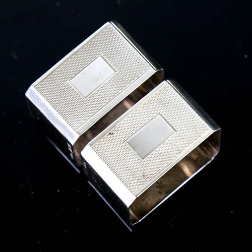 145 - A pair of Art Deco style Elizabeth II silver napkin rings, canted rectangular form with engine turne... 