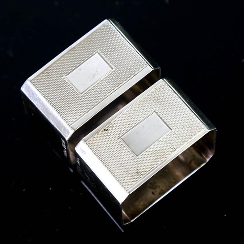 145 - A pair of Art Deco style Elizabeth II silver napkin rings, canted rectangular form with engine turne... 