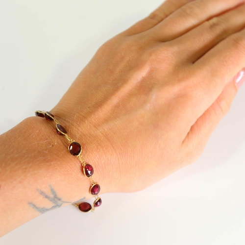 398 - A modern handmade 14ct gold garnet line bracelet, set with oval mixed cut garnets, bracelet length 1... 