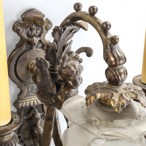 1463 - A pair of ornate bronze twin-branch wall light fittings, decorated with winged figures and frilled g... 